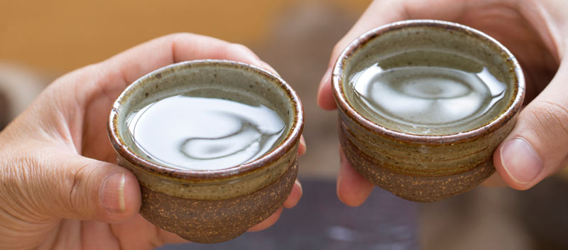 Two hands toasting with sake cups