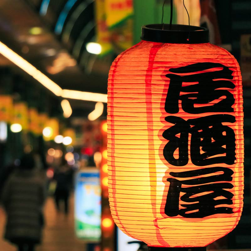 Izakaya lantern sign on a brightly lit street at night