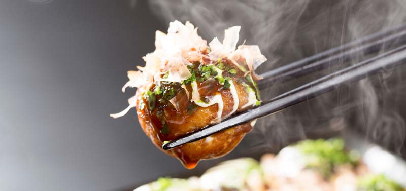 Takoyaki octopus ball held in chopsticks