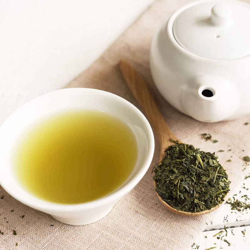Japanese green tea in a plain white cup with a teapot and loose green tea leaves