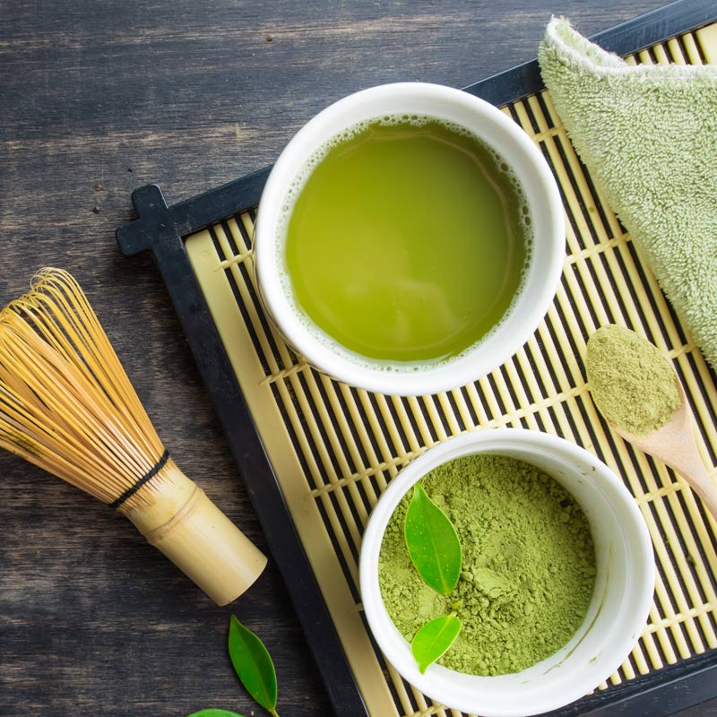 Vibrant green matcha tea in a Japanese tea bowl with powdered tea and a whisk on the side
