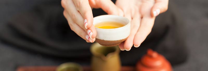 Hands serving green tea in a Japanese tea cup