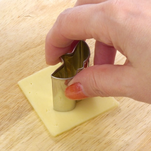 Stainless steel food cutter being pressed in to sliced cheese by hand