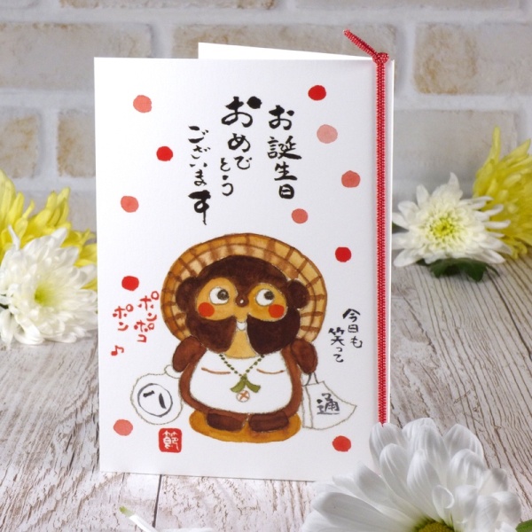 Japanese left-opening birthday card with tanuki character illustration on table top