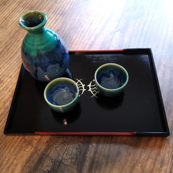 Blue ceramic sake jug and cups on black lacquered Japanese tray