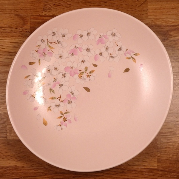Pale pink Japanese plate with pink and gold cherry blossom design on a wooden surface