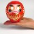 Red daruma doll held on the palm of a hand