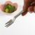 Hand holding mini picnic fork with veggie salad in the background