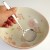 Hand holding Tsuchime stainless steel skimmer ladle over large ceramic bowl